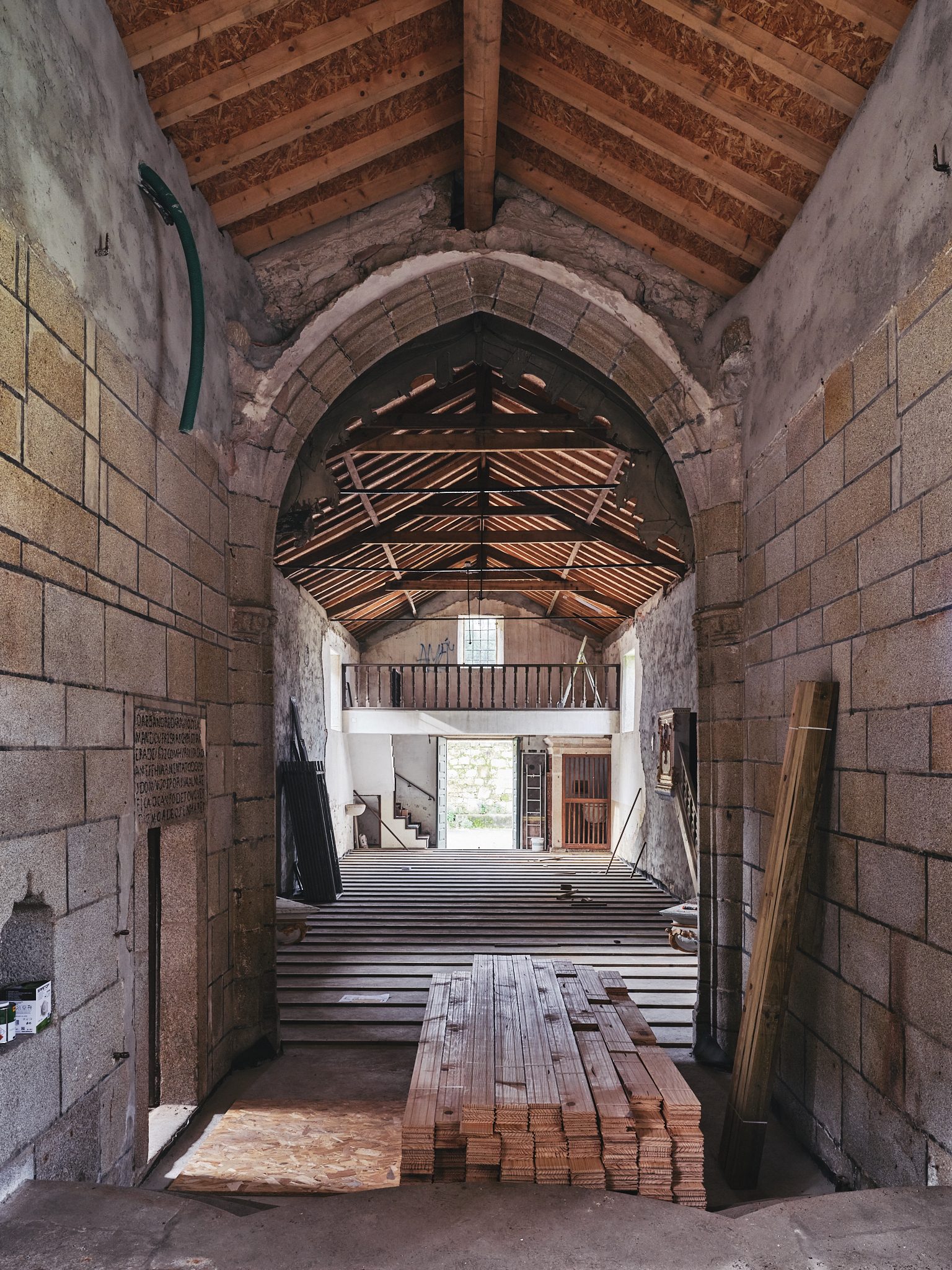 O interior em obra visto através do arco de pedra, com tábuas empilhadas no chão